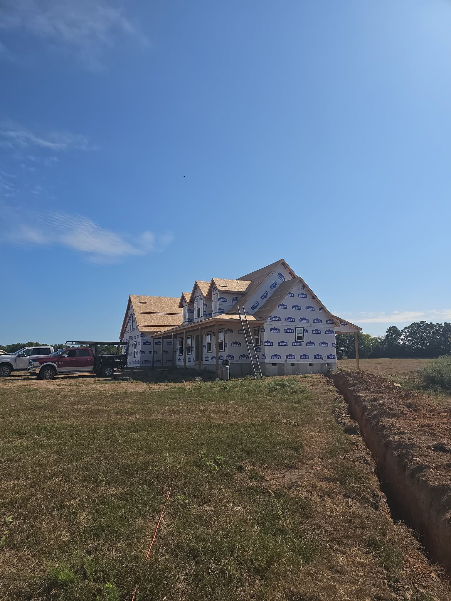 Partially built house with exposed framing on a sunny rural lot under a blue sky