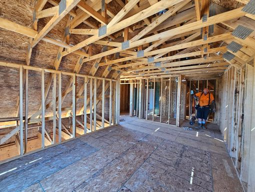 Unfinished attic with exposed wooden framing; two workers inspect the space near the far wall.