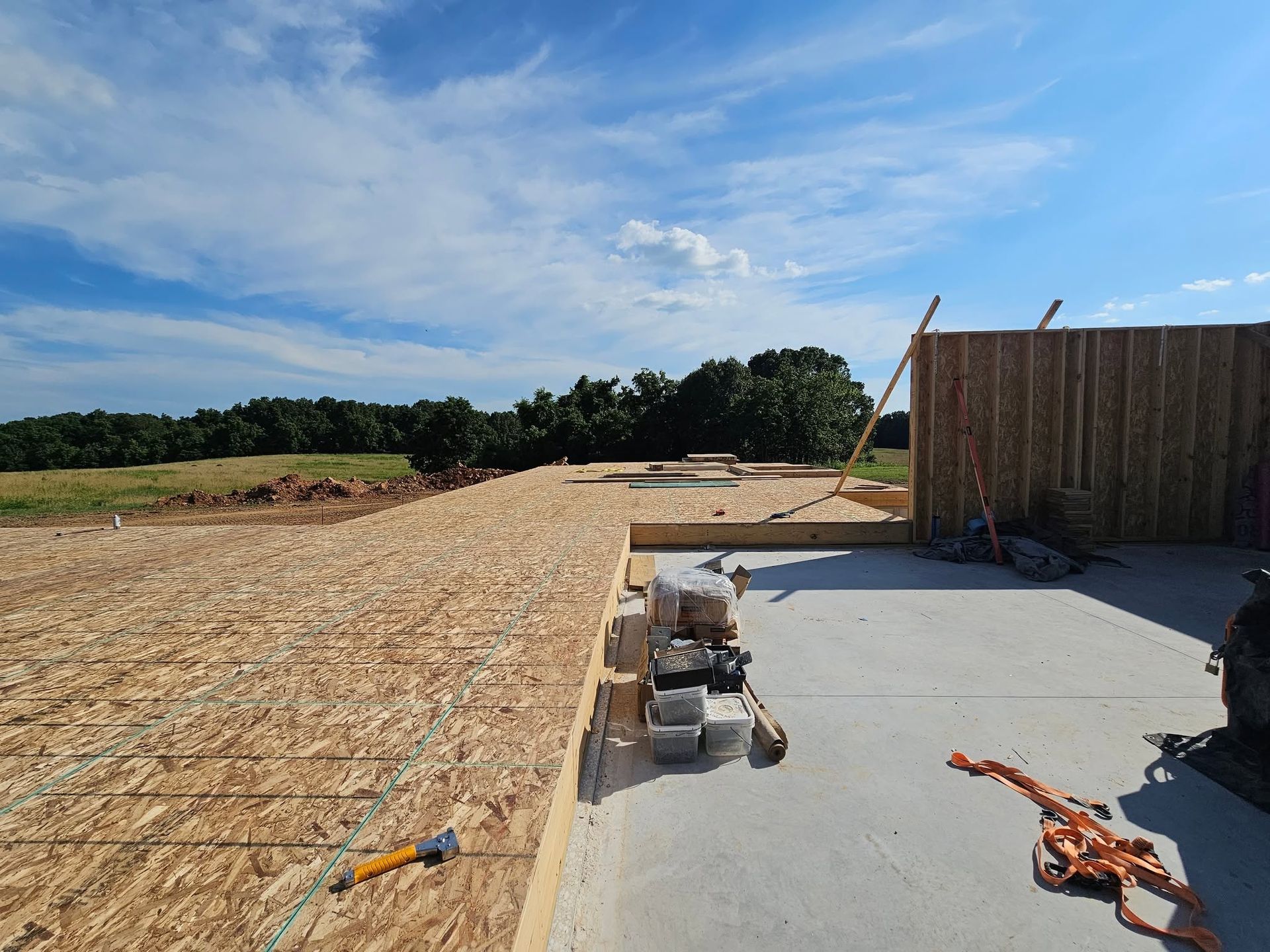 Partly built house foundation with wood framing, concrete slab, and tools under a blue sky