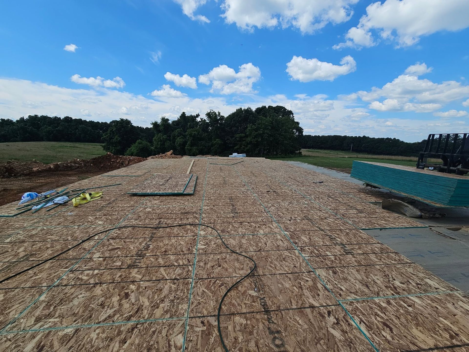 Roof under construction with plywood sheathing, blue sky, and trees in the background