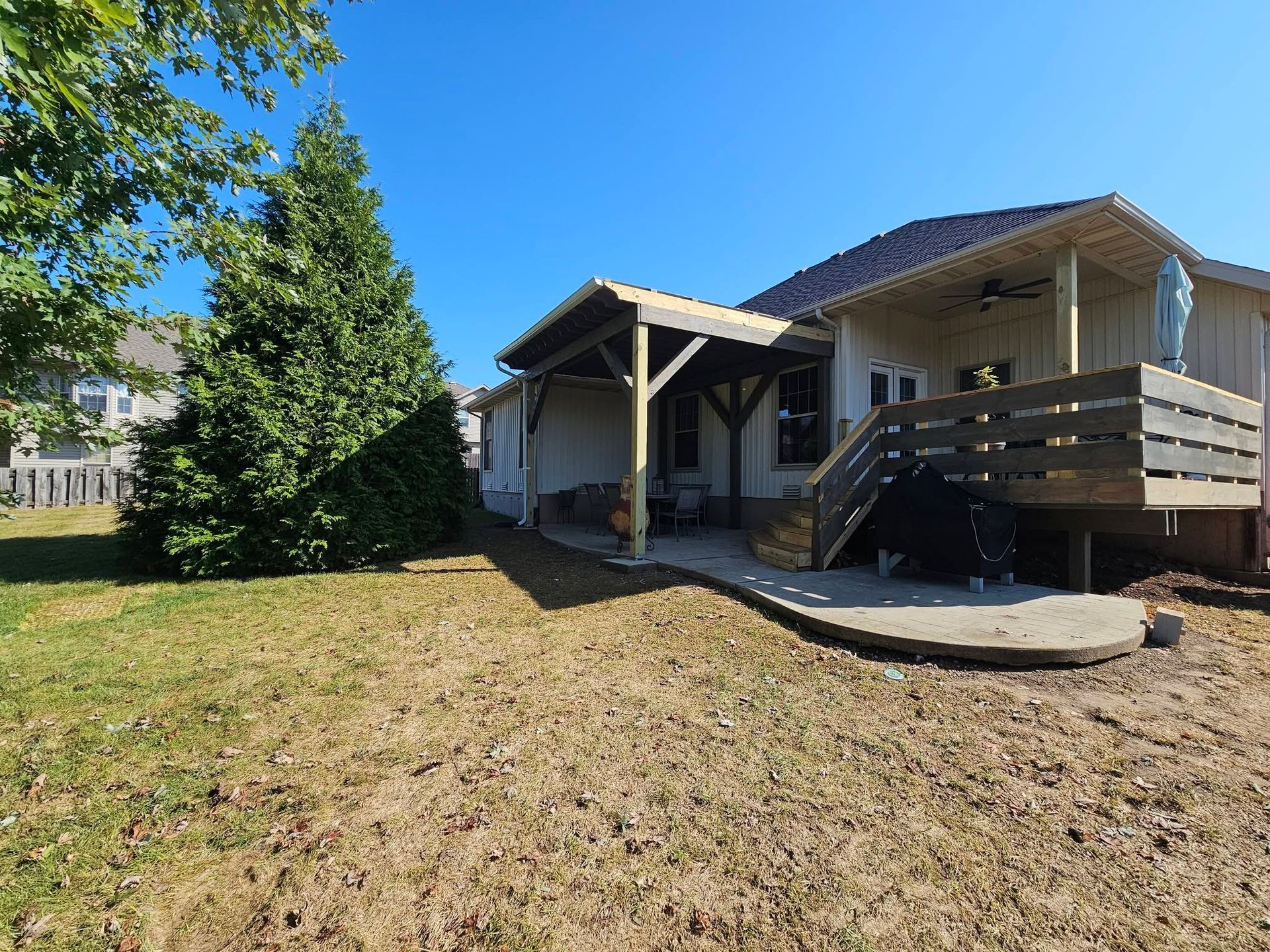 Single-story house with a covered porch and ramp, viewed from a dry grassy yard under a blue sky