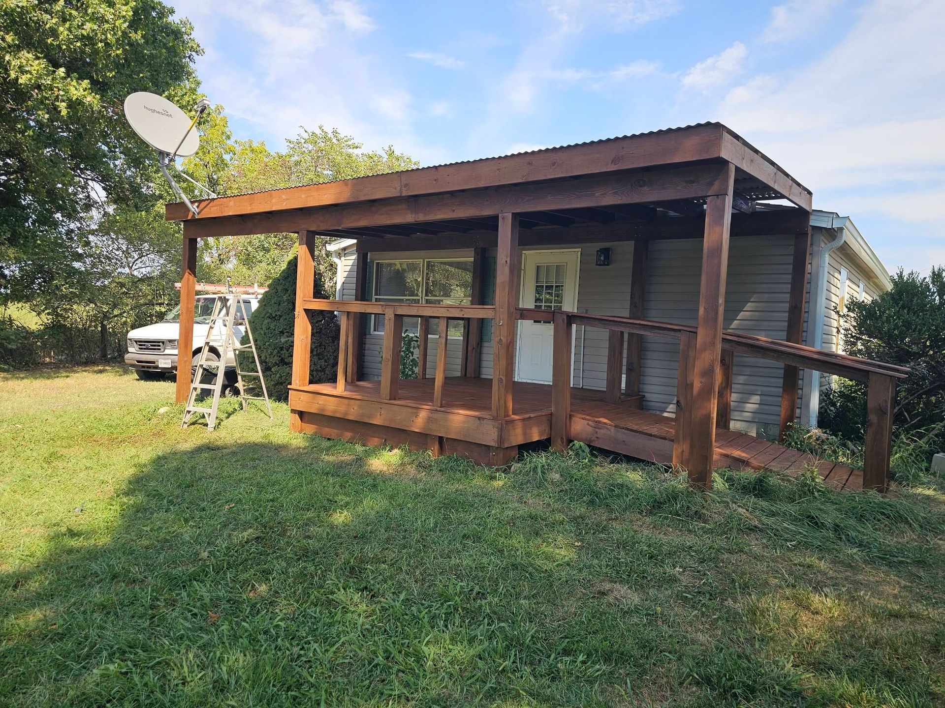 Small wooden porch house with a satellite dish, set in a grassy yard under a blue sky.