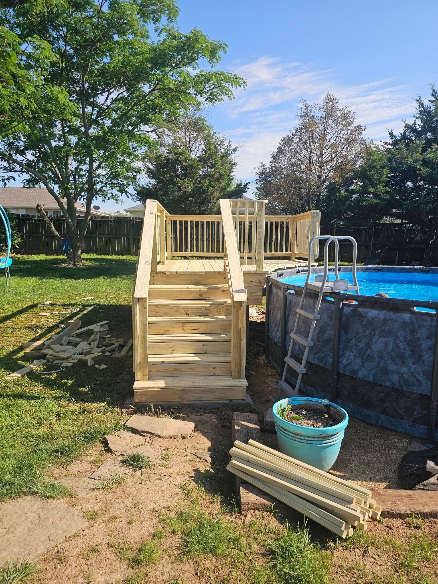 Wooden deck stairs and railing beside an above-ground pool in a sunny backyard