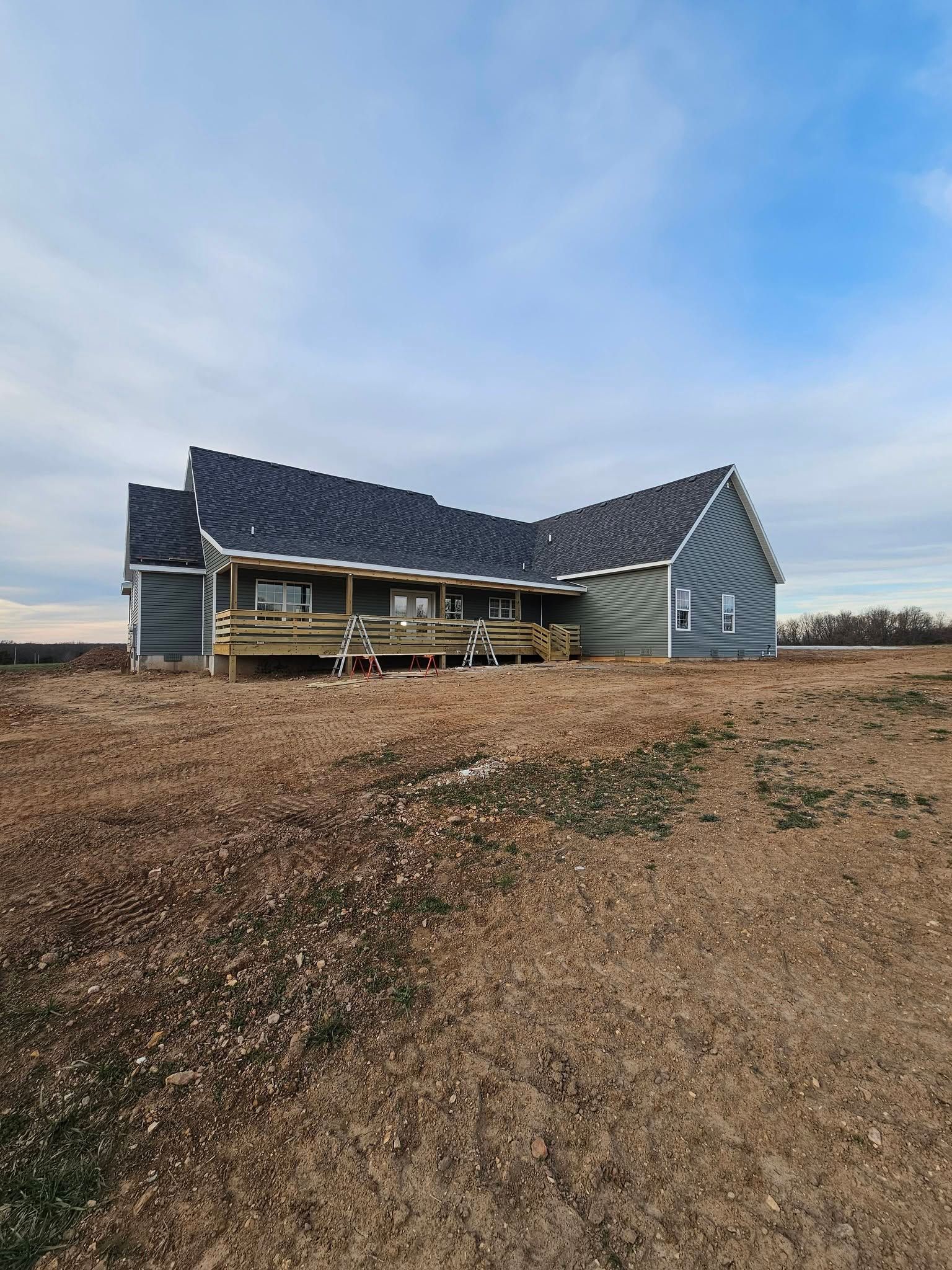Partially built house with dark roof on a barren field under a cloudy sky
