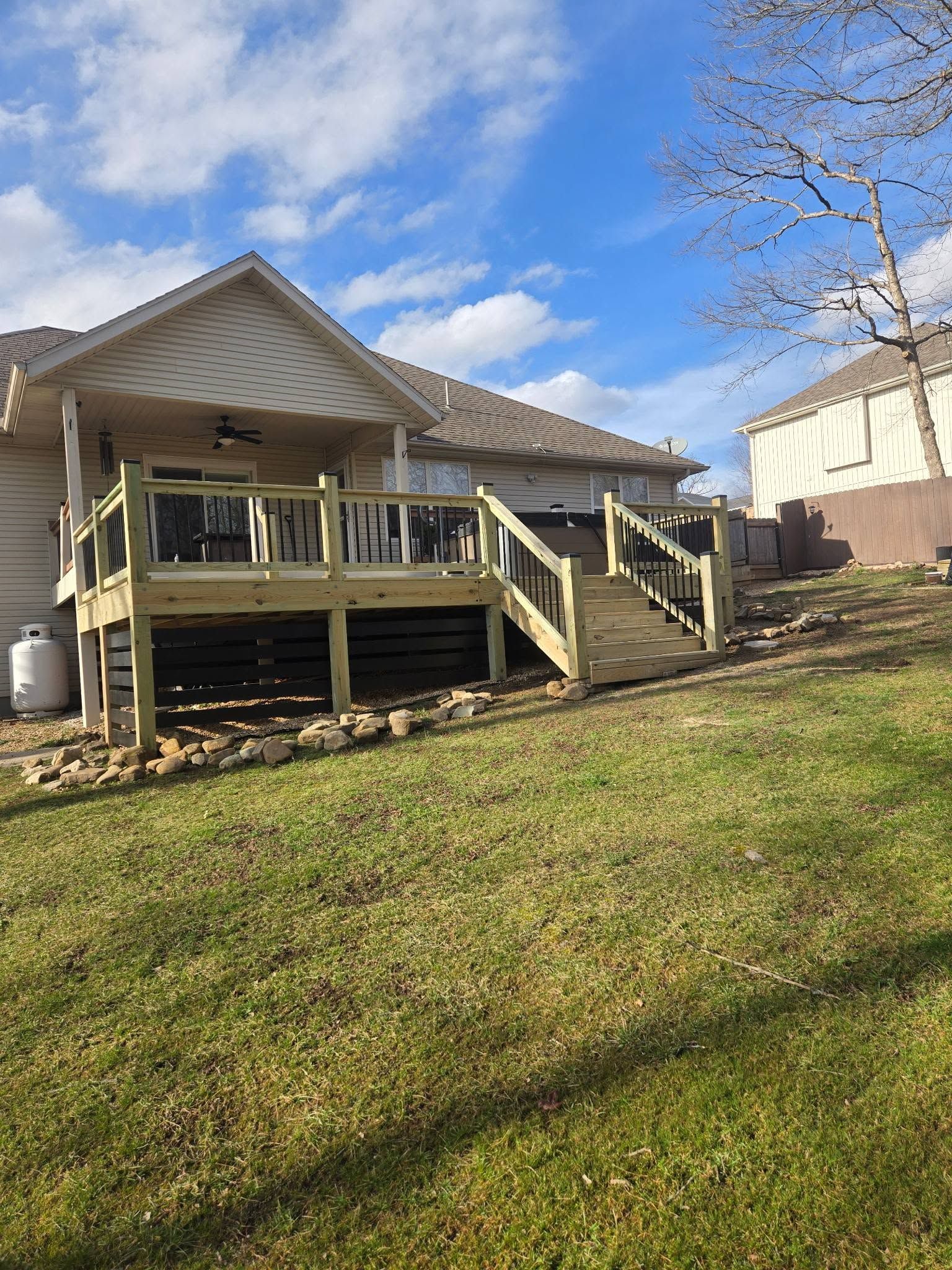 Single-story house with a wooden front porch and steps on a grassy yard under a blue sky