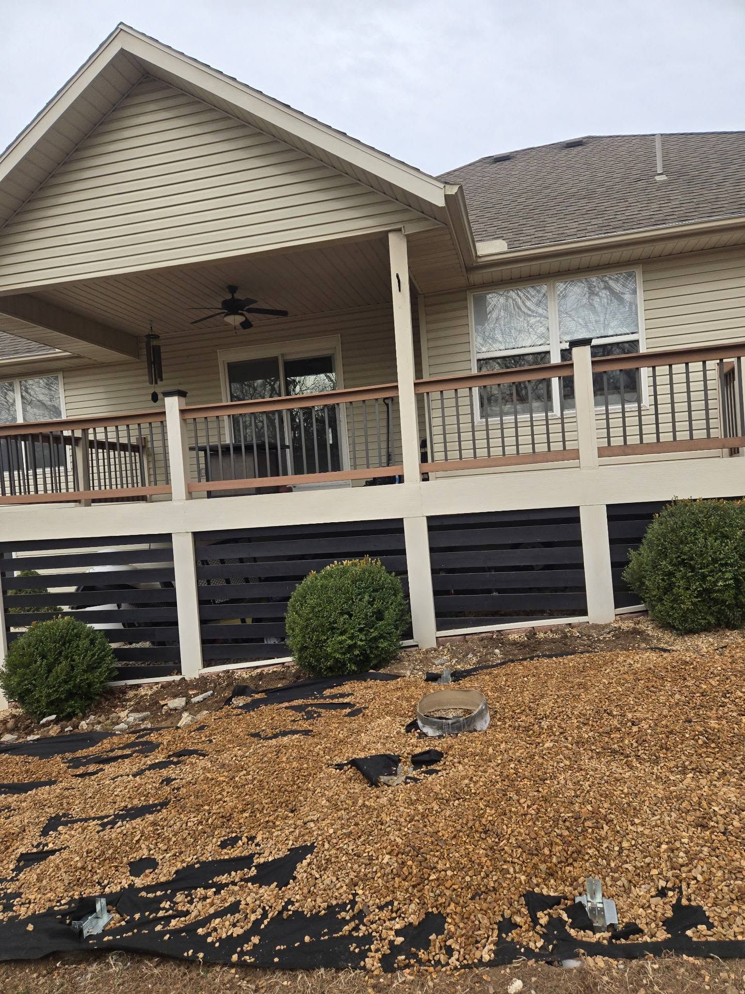 Suburban house porch with white railing, black skirting, and landscaped mulch front yard.