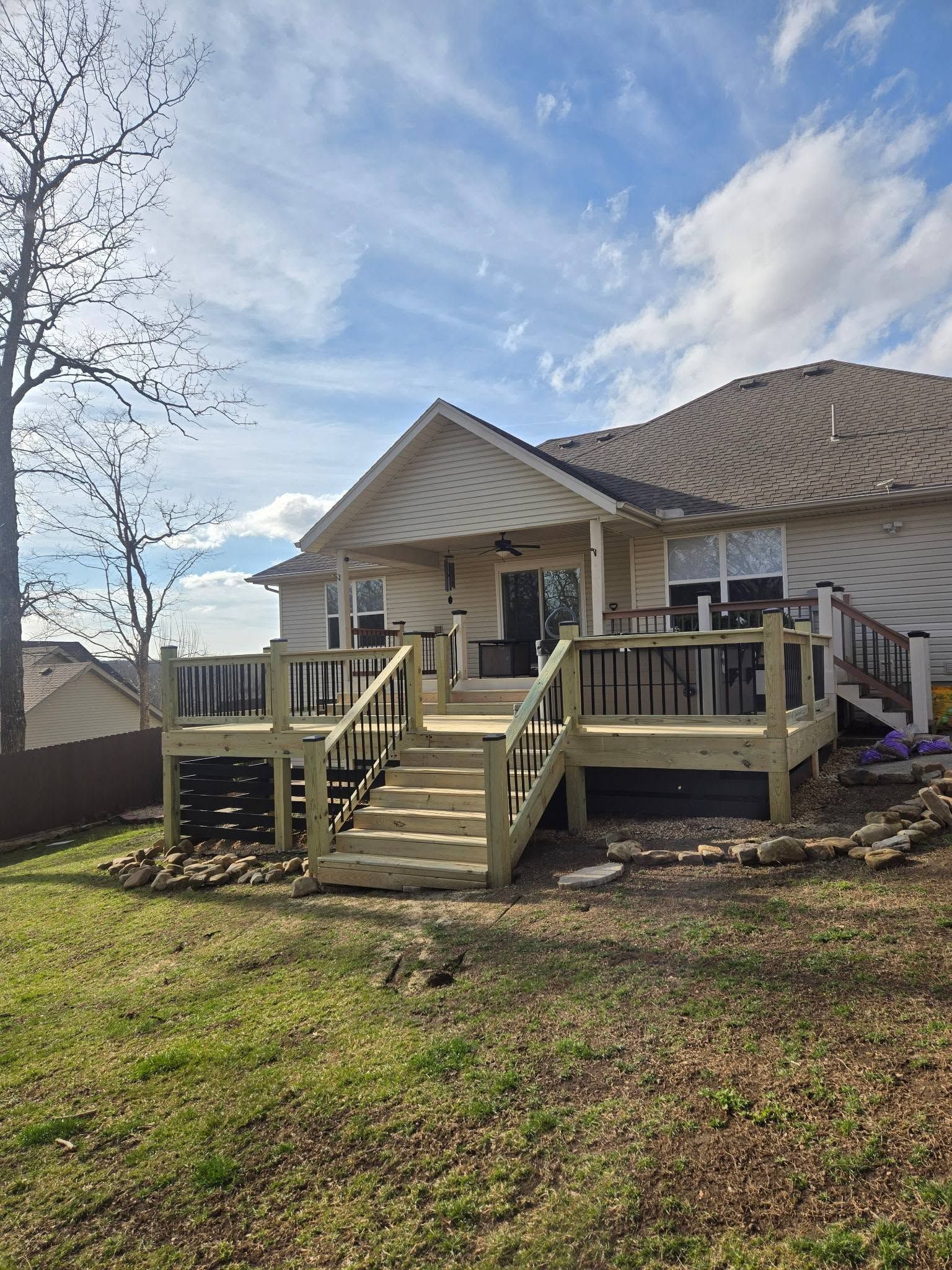 Back porch with wooden steps and railing on a house in a grassy yard under a cloudy sky