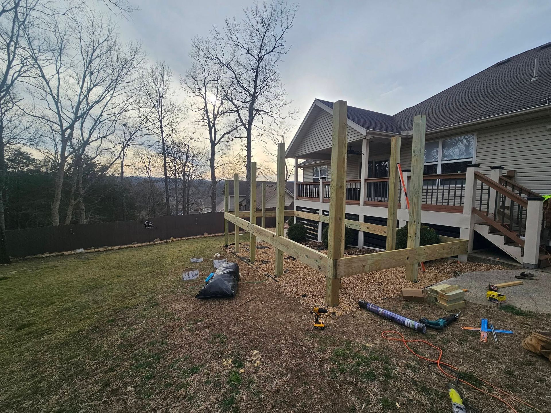 Backyard deck under construction beside a house, with lumber, tools, and a grassy yard.