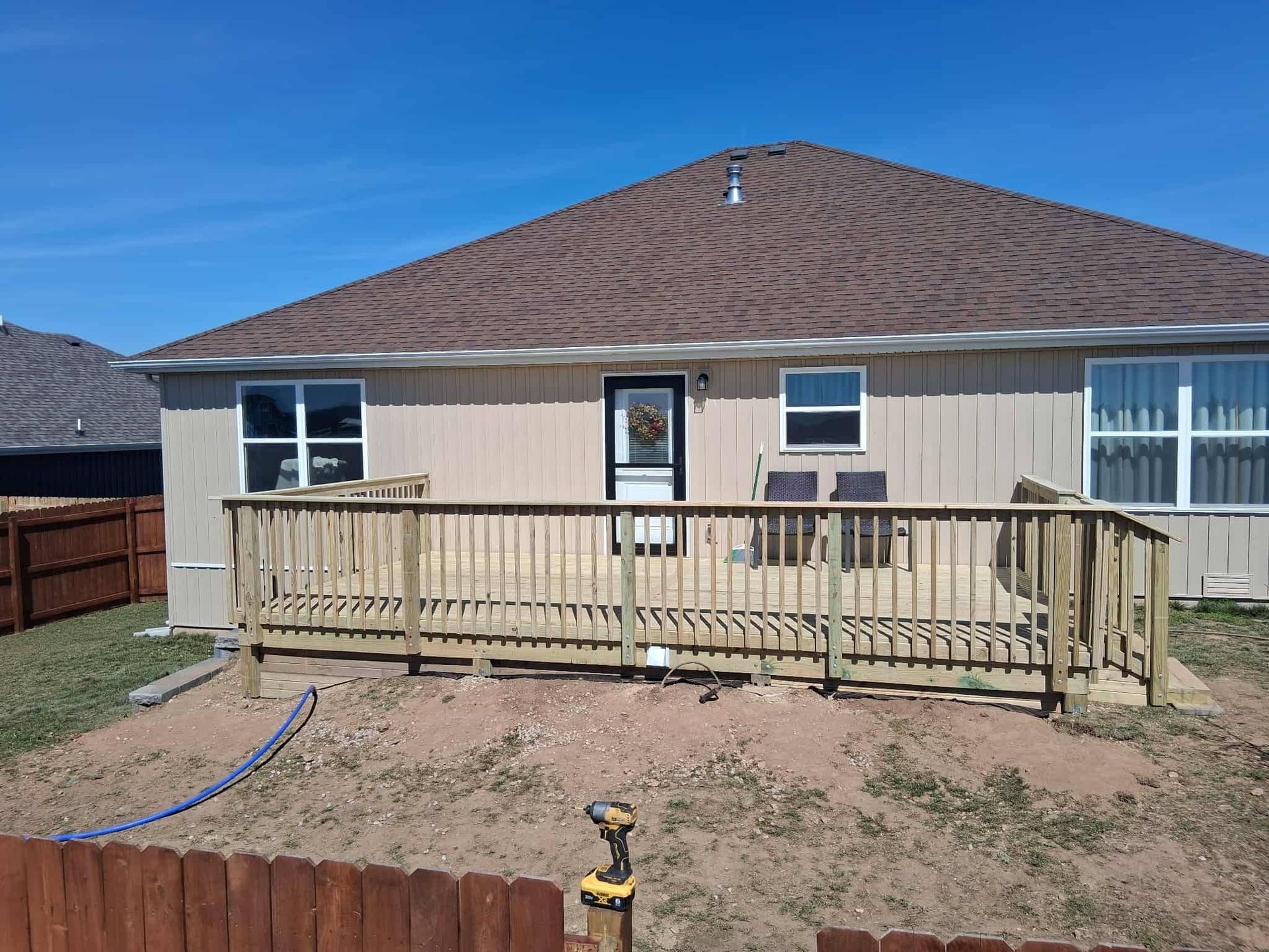Single-story tan house with a wooden deck and fenced yard under a clear blue sky