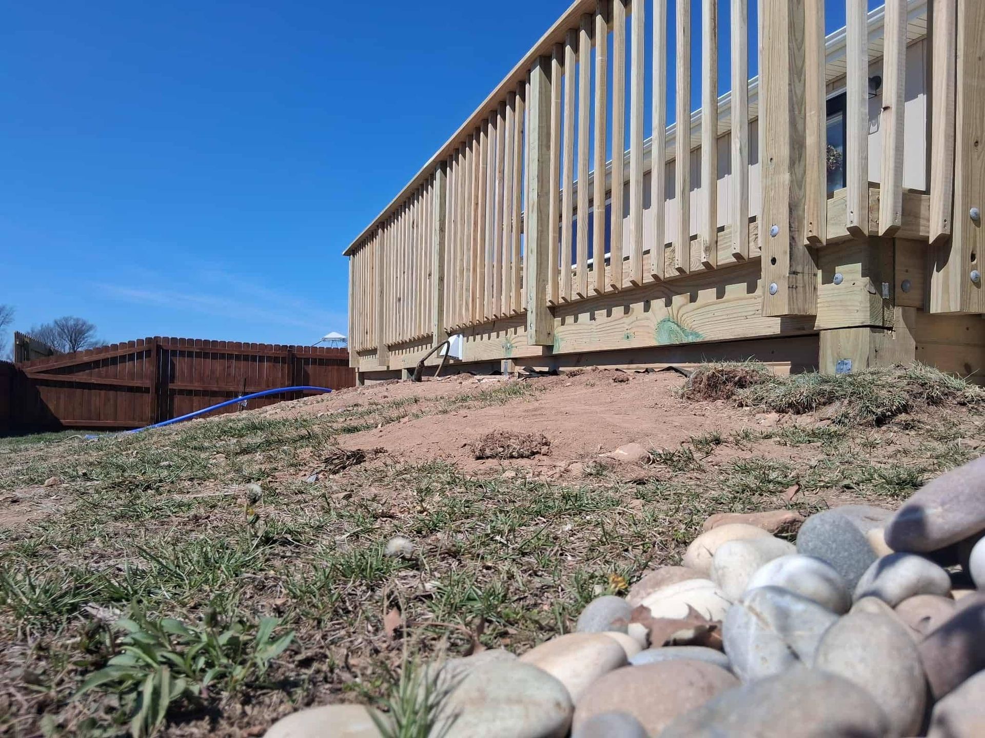 Wooden deck railing above a rocky, grassy slope under a clear blue sky