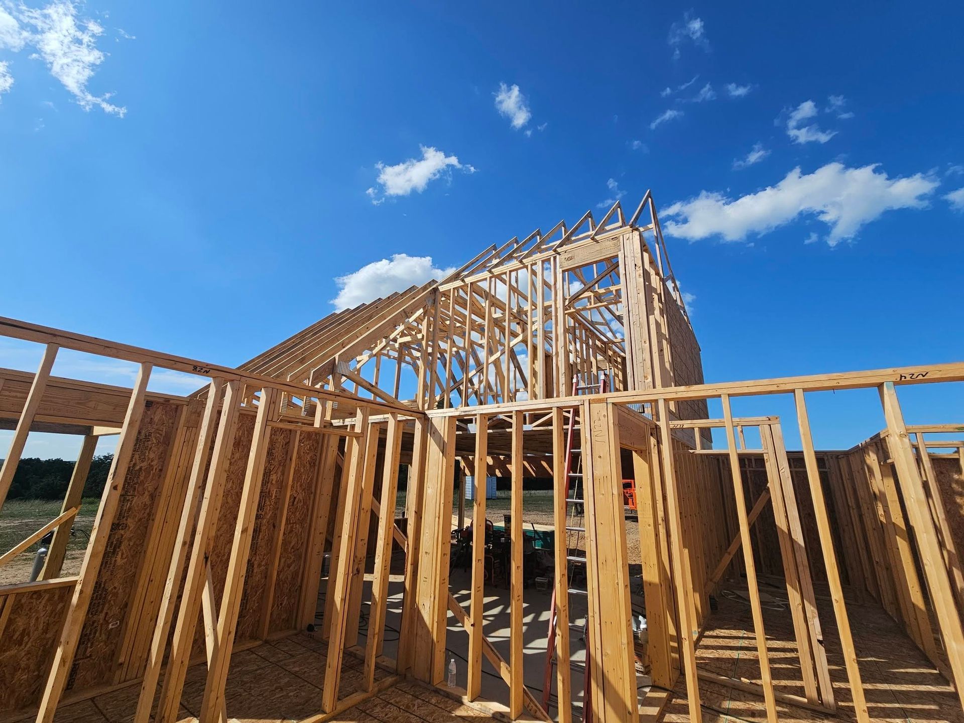 Wooden house framing under construction against a bright blue sky with scattered clouds