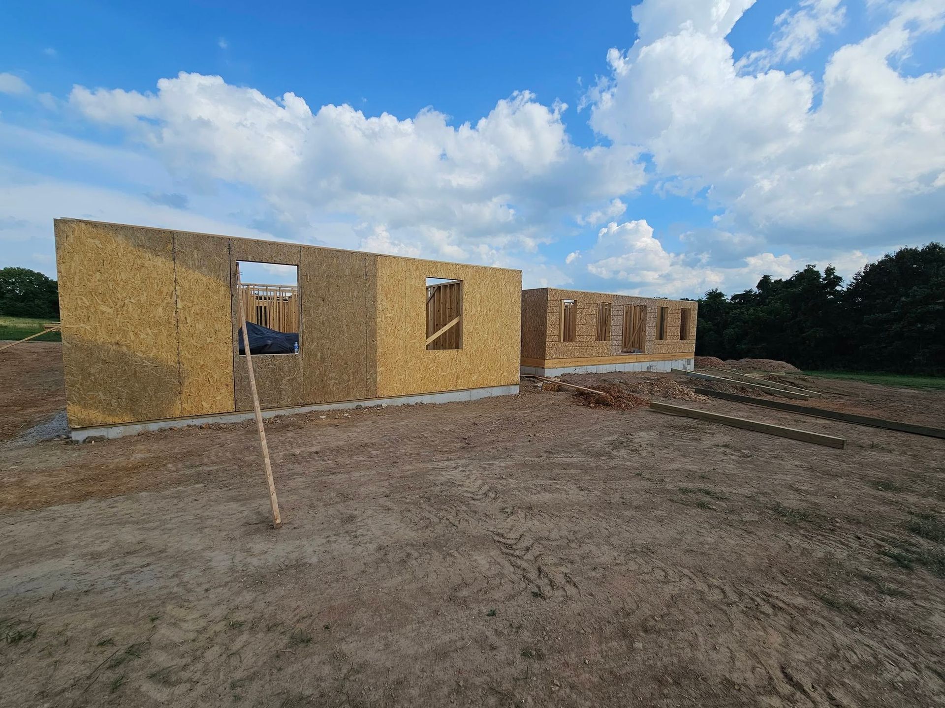 Partially built house with wood framing on a dirt lot under a cloudy sky