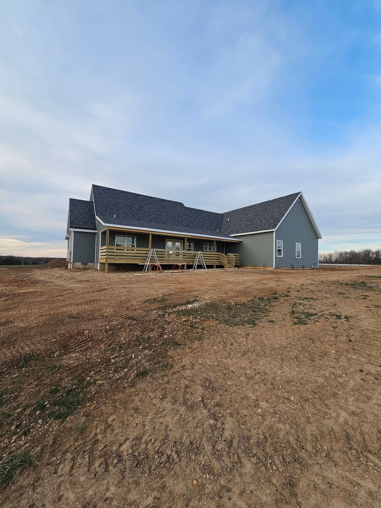 Partially built house with roof shingles and exposed framing on a bare lot under a cloudy sky