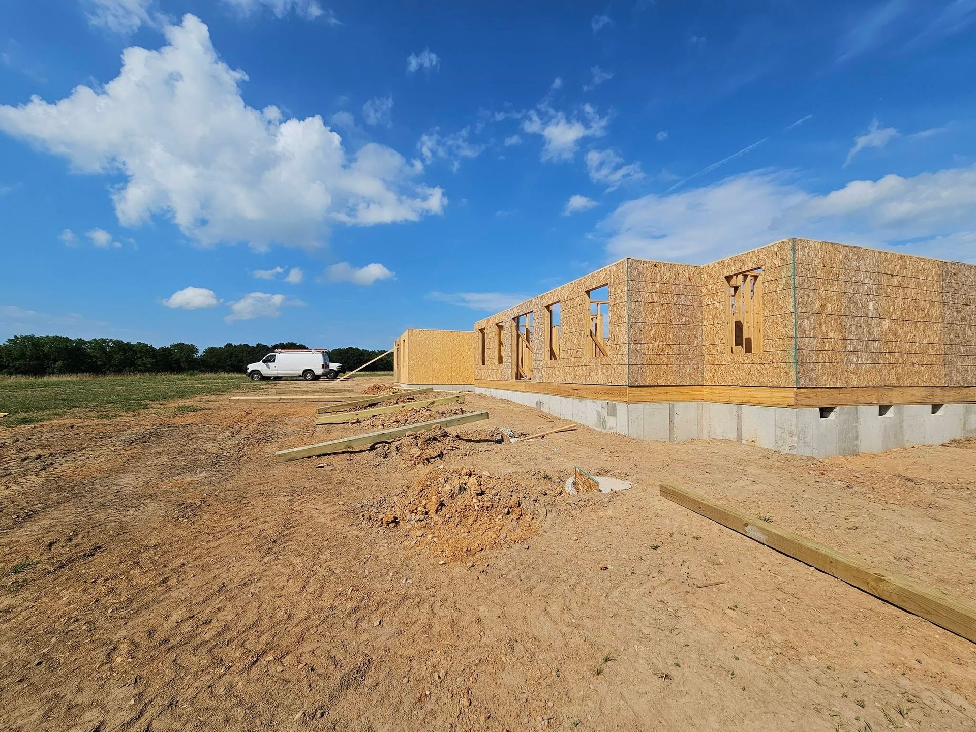 Partially built brick structure on a dirt lot under a blue sky with scattered clouds