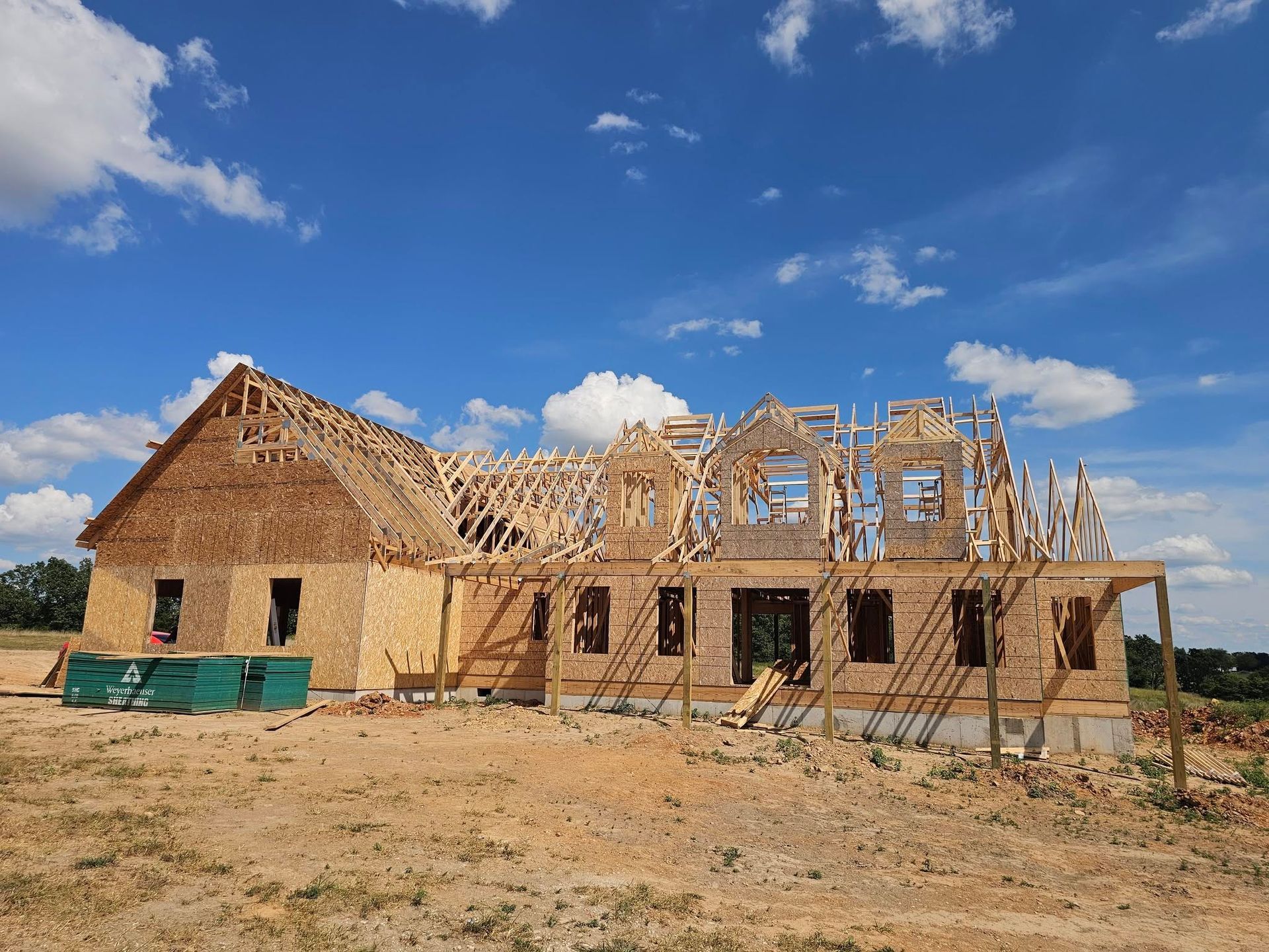 Partially built brick house under construction on a dry lot, with roof trusses and blue sky