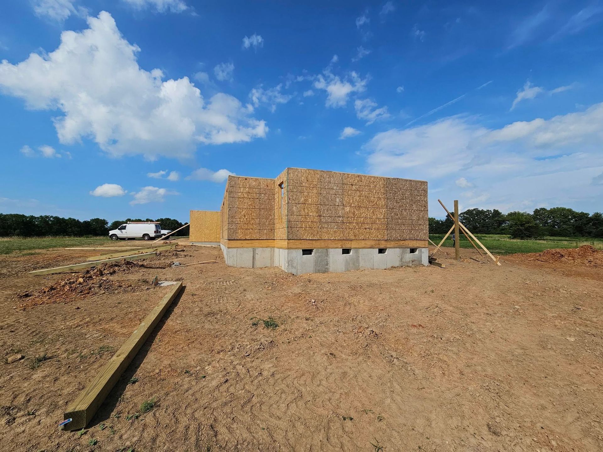 Partially built brick structure on a dirt lot under a bright blue sky with clouds