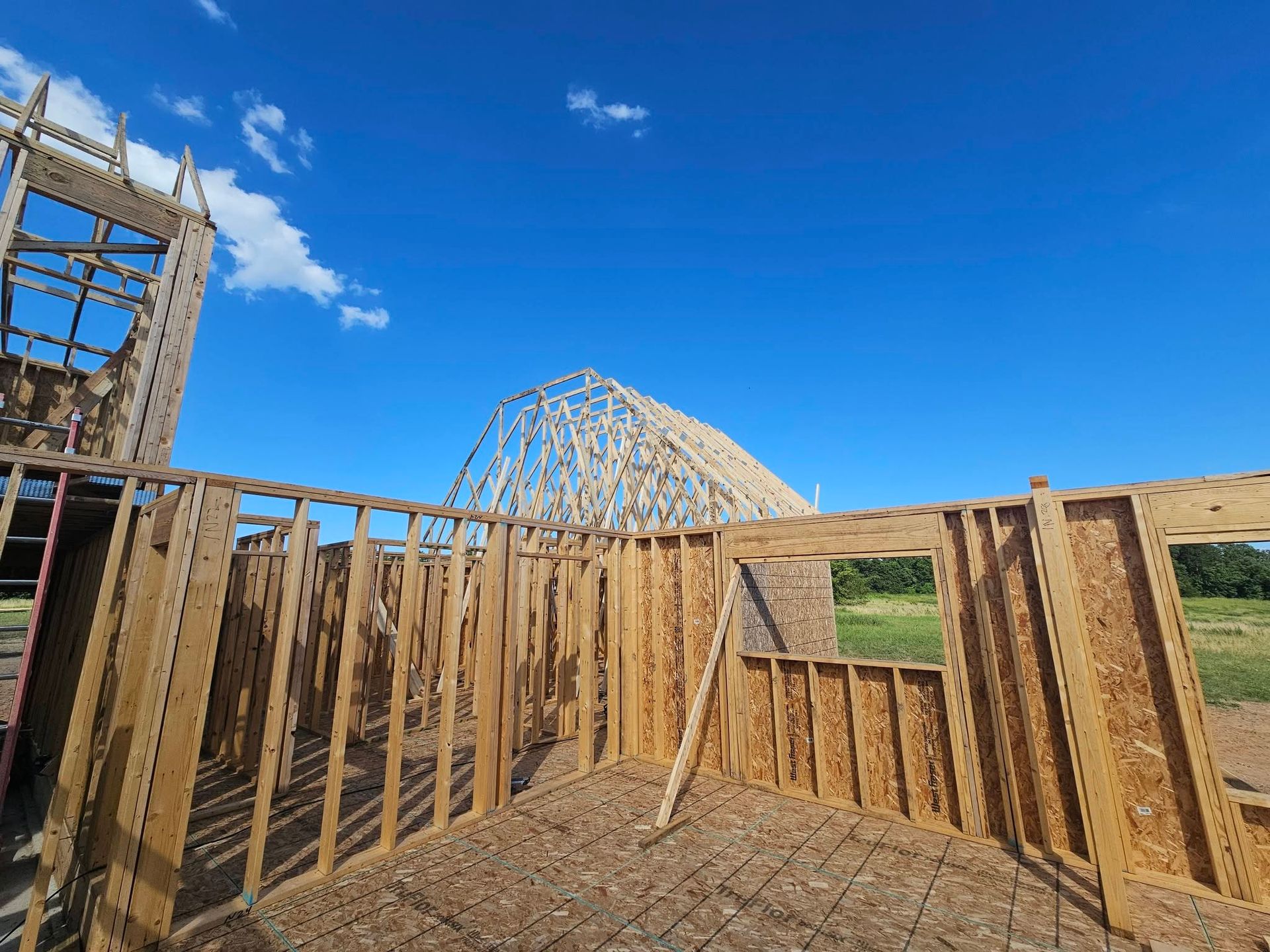 Wooden house framing under construction on a sunny day with blue sky and hills in the background