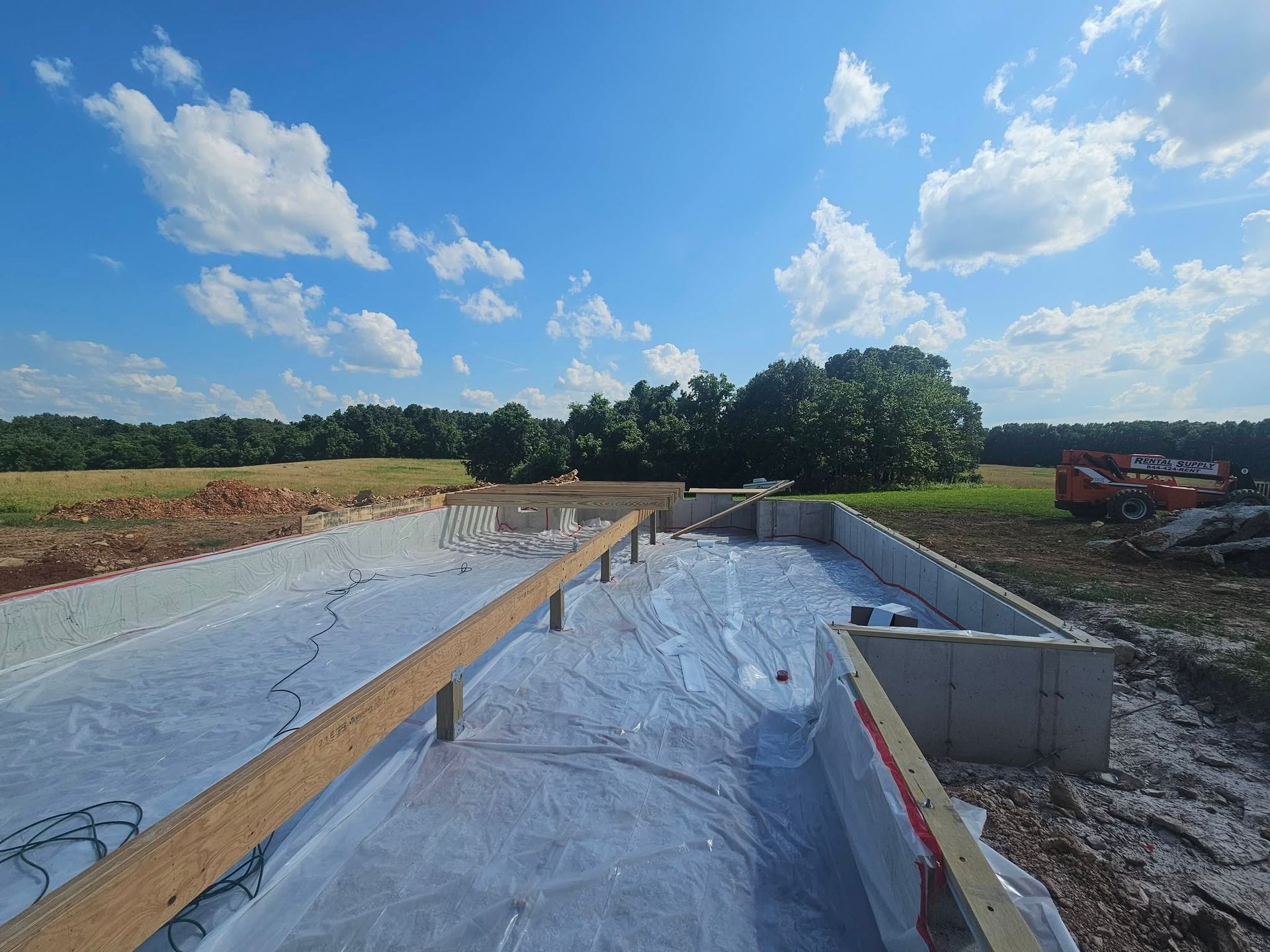 Construction site with concrete channel and plastic sheeting under a bright blue sky