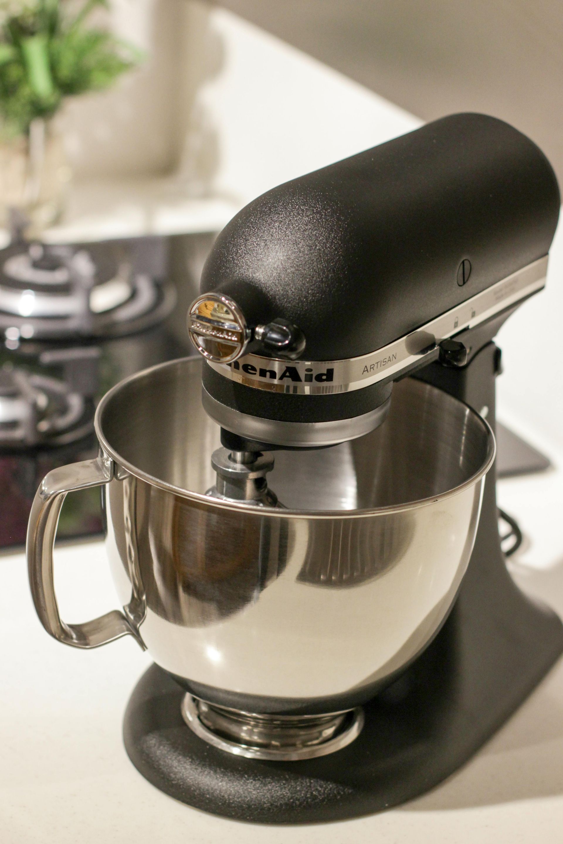 Black KitchenAid stand mixer with stainless steel bowl, on a white countertop.