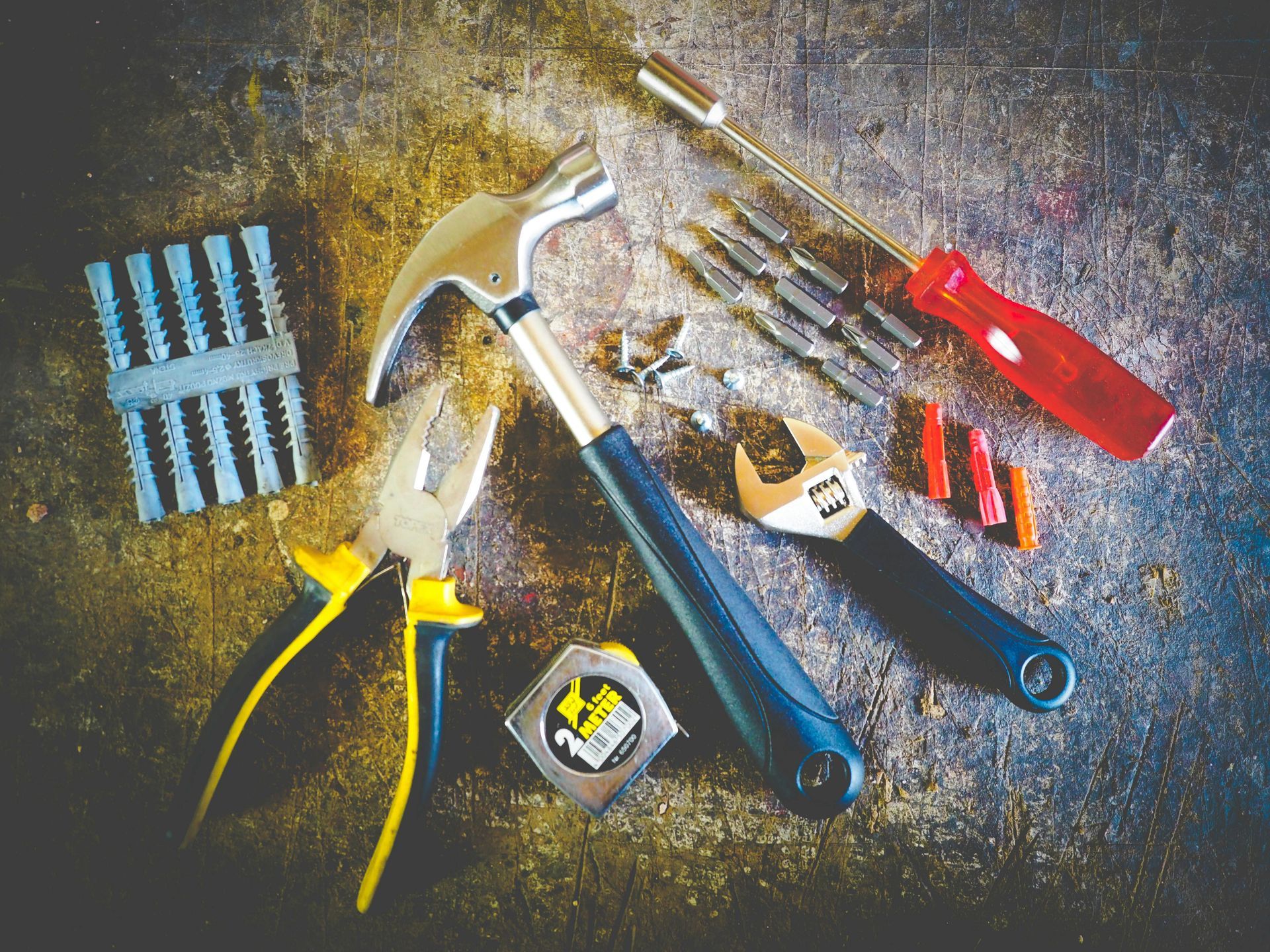 Various hand tools, including a hammer, pliers, and screwdriver, are arranged on a textured surface.