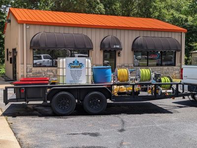 Trailer loaded with cleaning equipment parked in front of a tan building with black awnings.