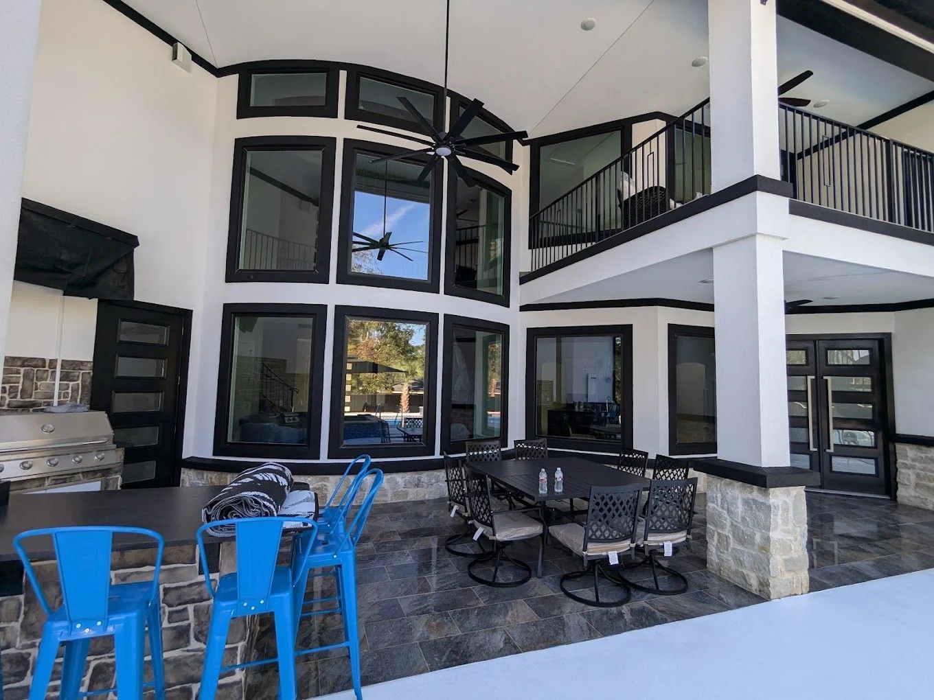 Modern patio with blue chairs, black tables, and a two-story building with large windows.
