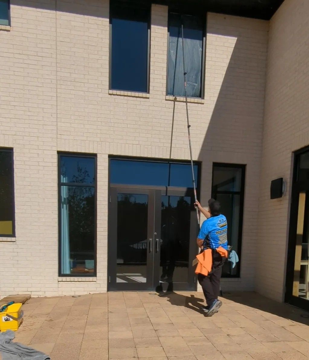 Person using a long pole to inspect a two-story beige building exterior near a glass door.