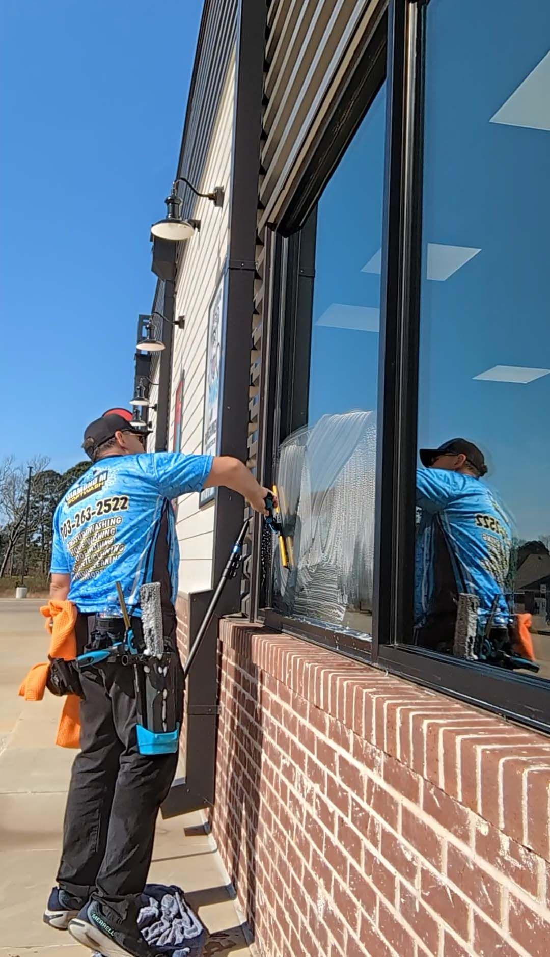 Worker in blue shirt inspecting exterior brick wall and window on a sunny day