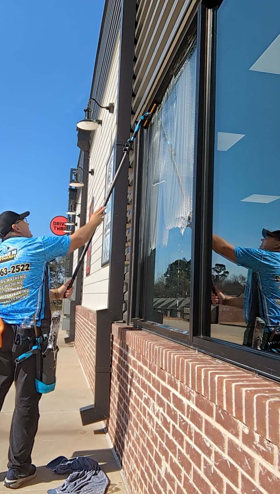 Worker using a long pole to clean or adjust the exterior of a brick building with large windows.
