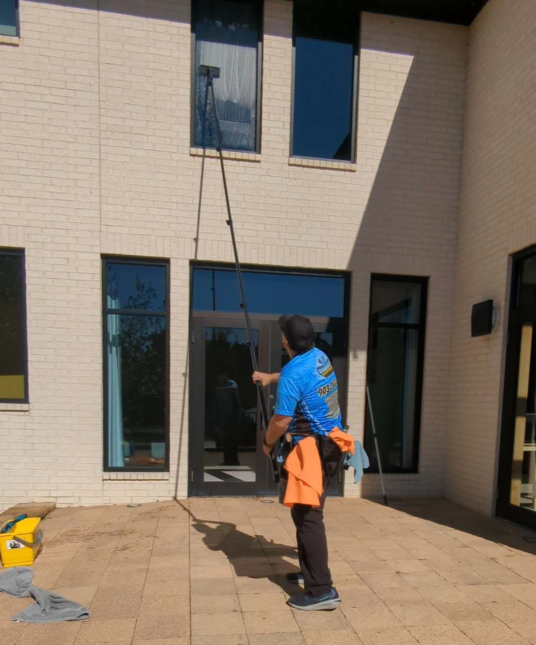 Person in blue and orange stands in a courtyard, looking up at a rope hanging from a building window.