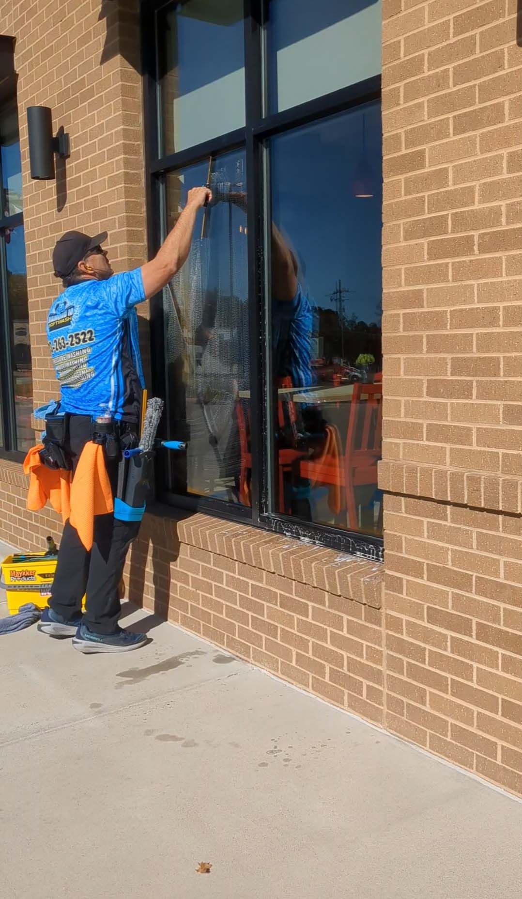 Person cleaning a storefront window with a squeegee beside a brick building