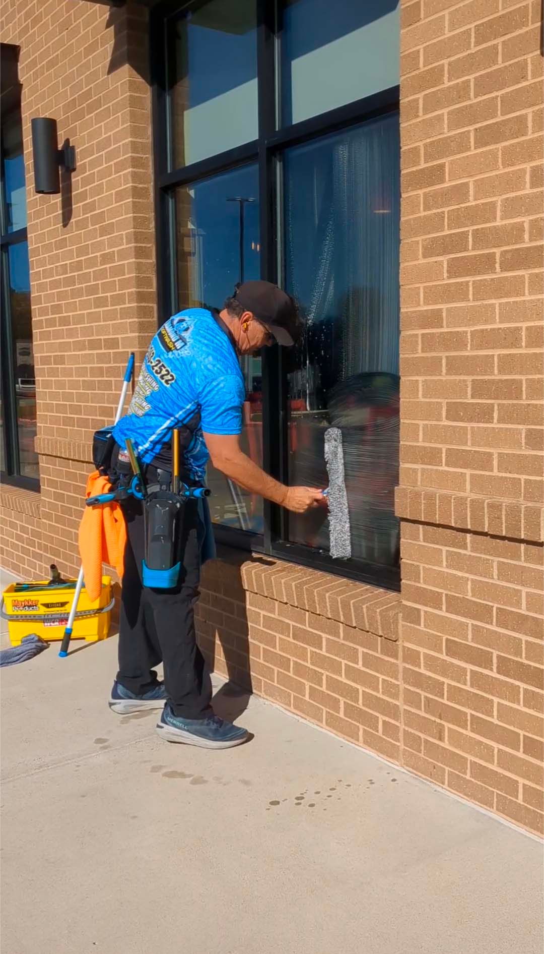 Worker in blue shirt cleaning a brick storefront window with a squeegee