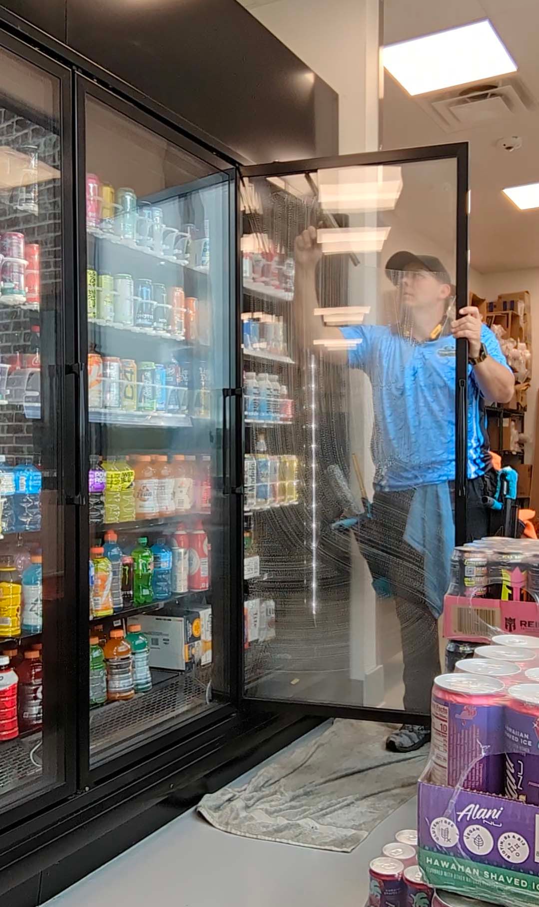 Person opening a glass freezer door in a convenience store aisle, with drinks and snacks visible.