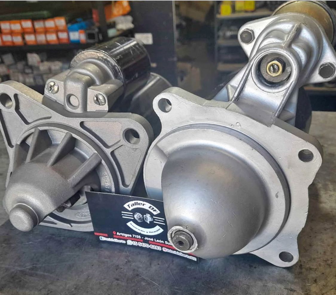 Dos motores de arranque automotrices plateados sobre un banco de trabajo con un fondo de taller.