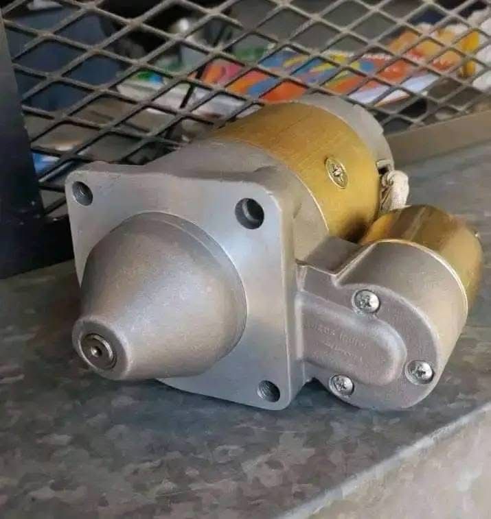 Primer plano de un pequeño motorreductor metálico con carcasa plateada y cuerpo de latón sobre una superficie perforada.