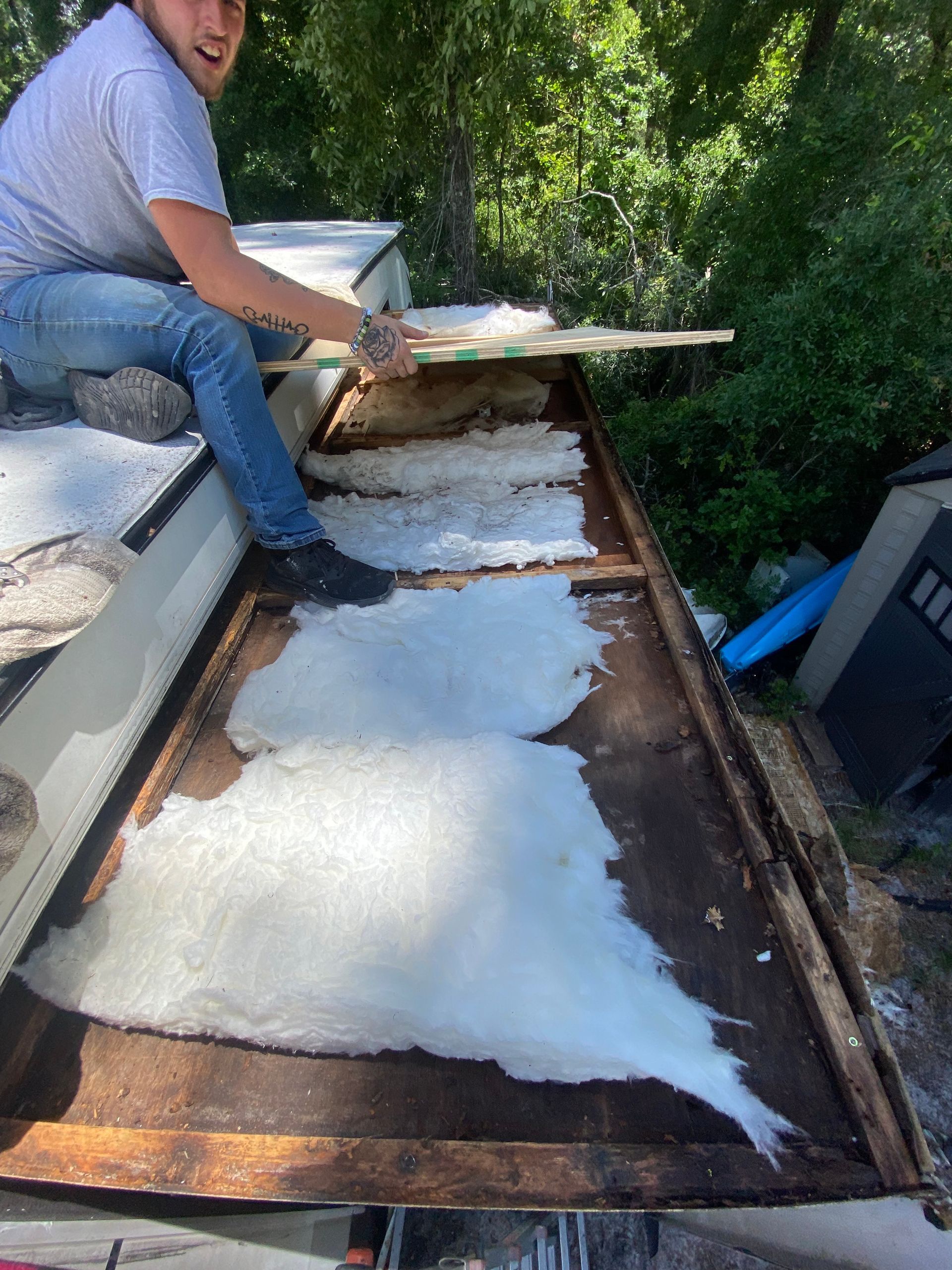 Man removing insulation from a roof structure outdoors.