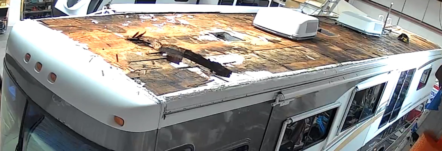 A damaged RV inside a warehouse, roof showing significant deterioration.