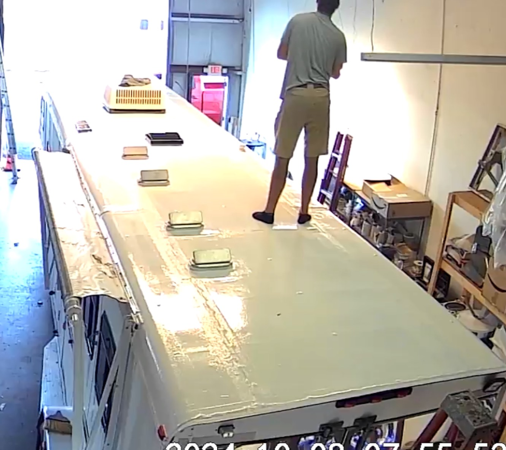 A person stands on the roof of a large vehicle in a cluttered indoor space.
