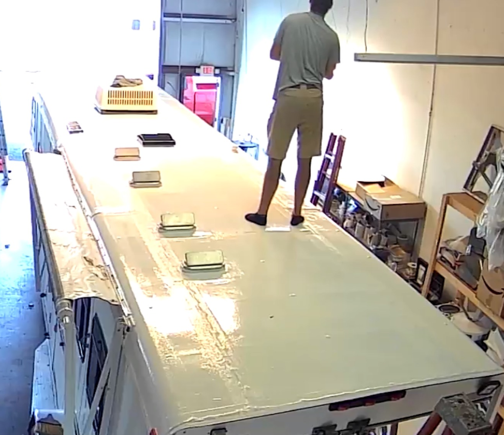 A person stands on the roof of a large vehicle in a cluttered indoor space.
