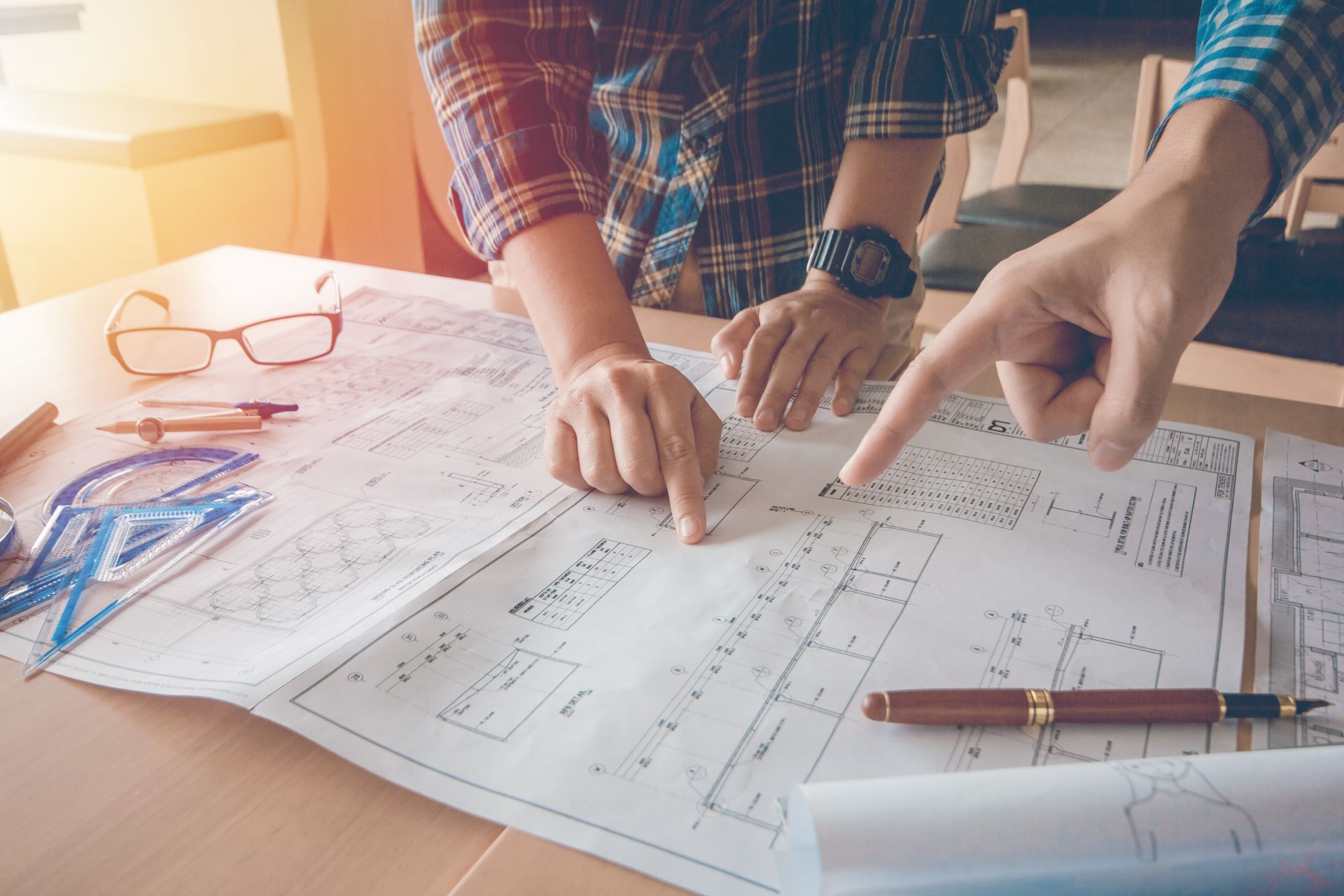 Custom home builder team pointing at layout blueprints on a sunlit studio desk.