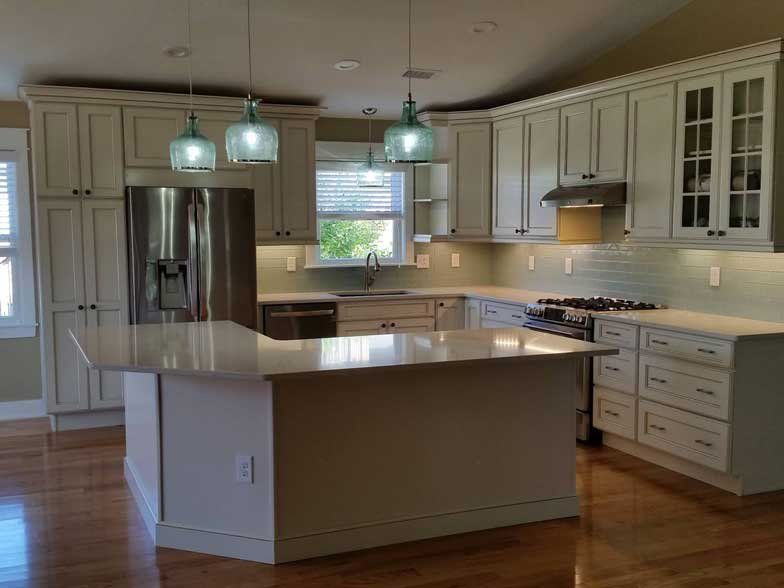 A modern kitchen featuring off-white cabinets, stainless steel appliances, an island with pendant lights, and wood floors.