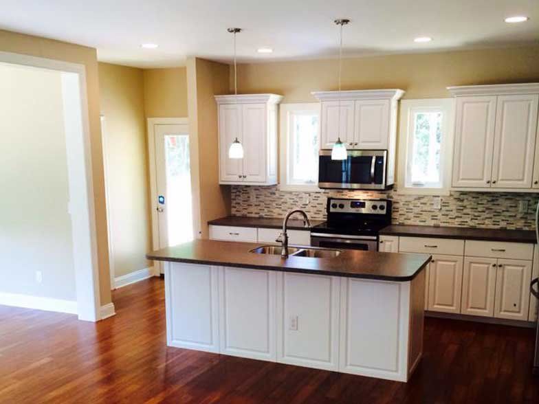 Modern kitchen with white cabinets, dark countertops, a center island with a sink, and hardwood floors.