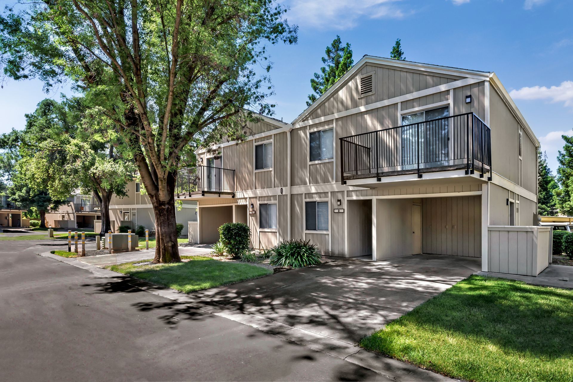 Apartment complex with green lawn, trees, and a partly cloudy blue sky.
