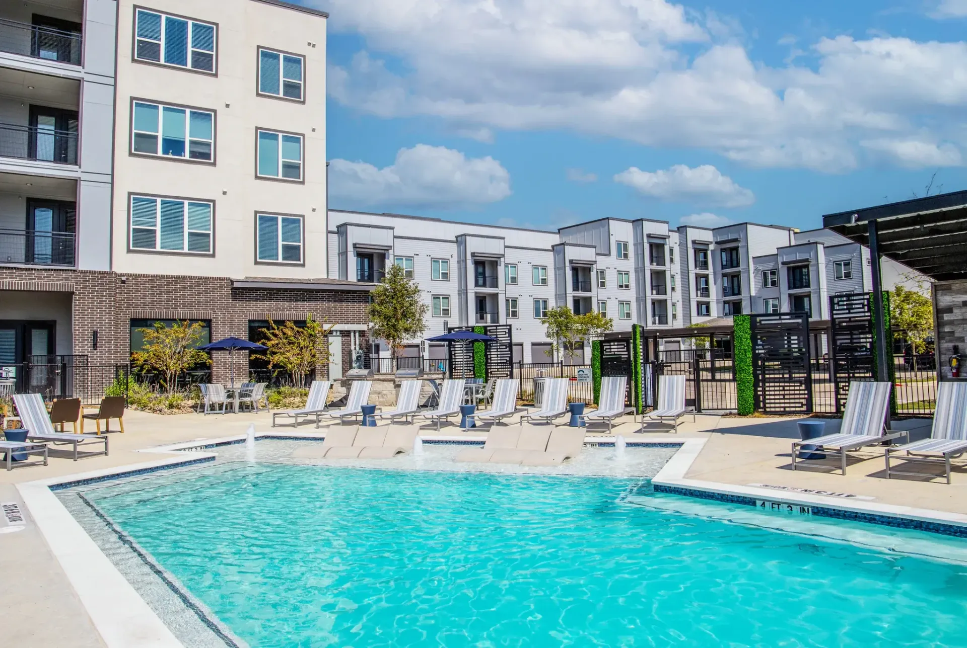Outdoor communal pool area with turquoise water, white lounge chairs, and surrounding modern apartment buildings.