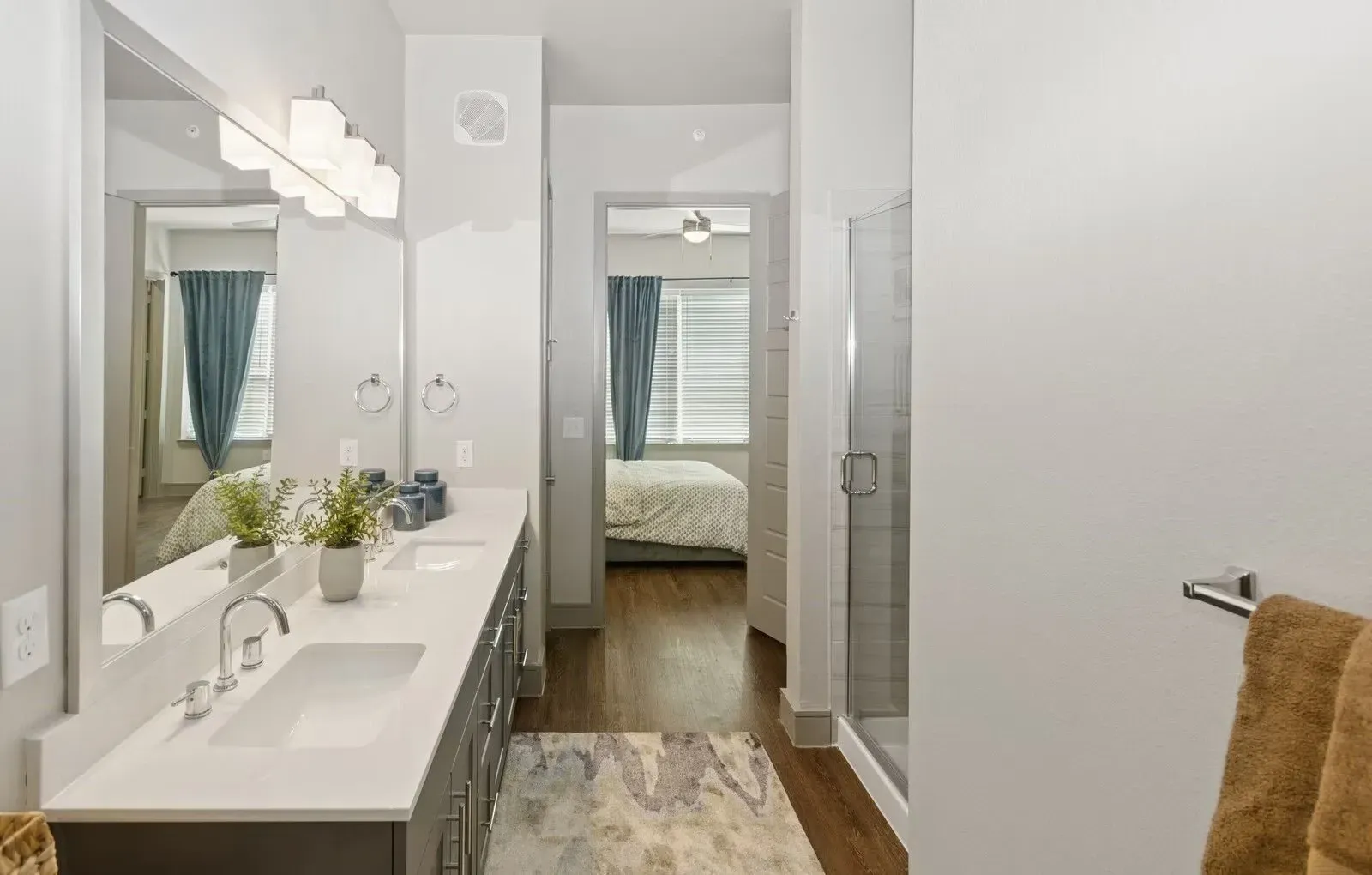 Modern apartment bathroom with double sink vanity, mirrors, and a glass-enclosed shower.