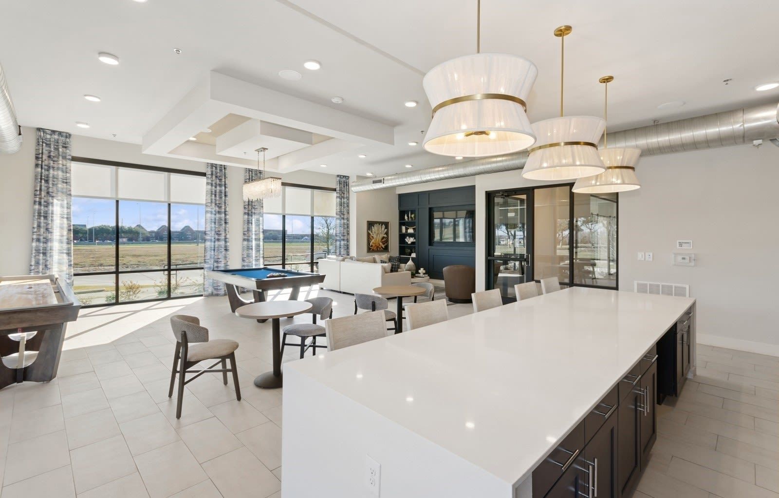 Bright community clubhouse with large windows, a pool table, and seating around a long white island.