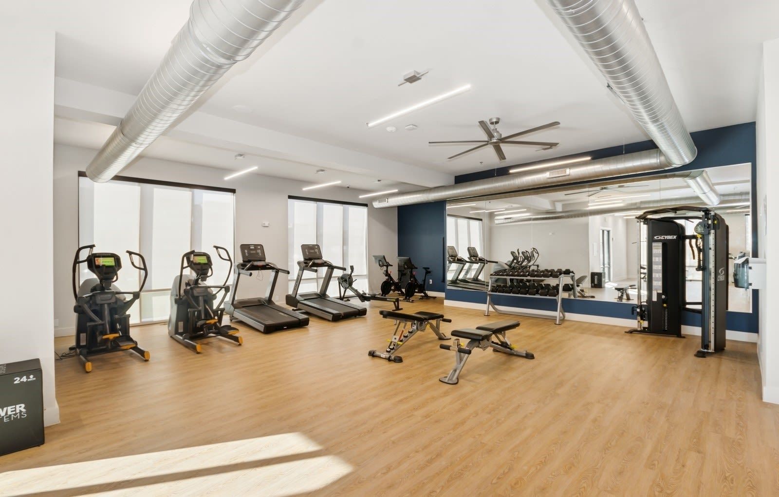 Bright apartment fitness center with cardio machines, free weights, and a large wall mirror.