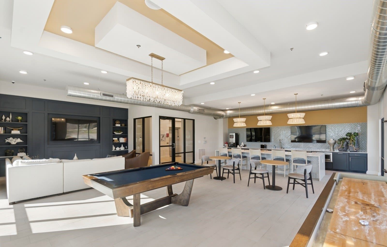 Spacious modern community lounge with a pool table, seating, and a coffee-bar area.