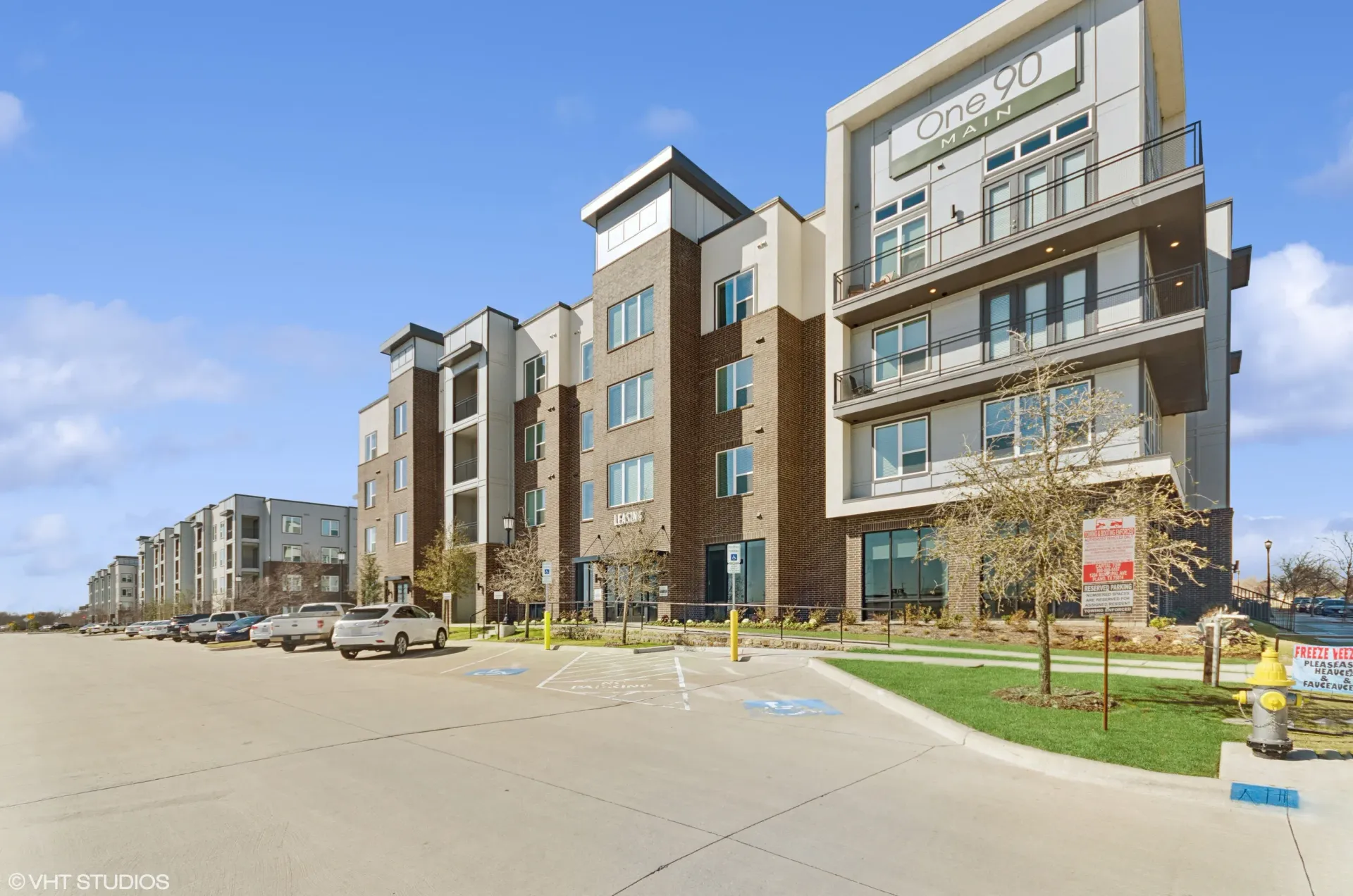 Exterior view of a modern apartment building with balconies and a parking lot.