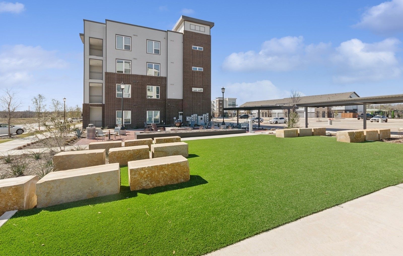 Exterior view of a modern apartment building with a green lawn and stone seating.